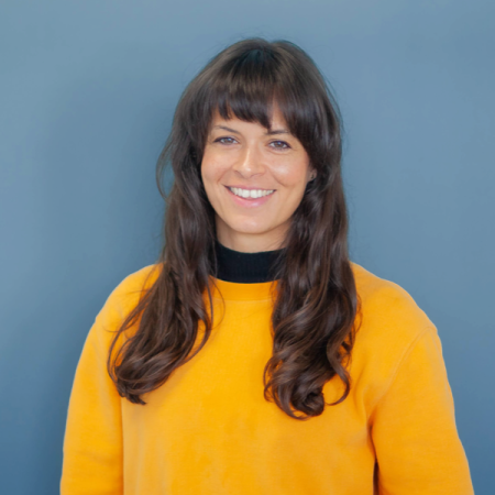 Bianca wears a yellow jumper and smiles at the camera